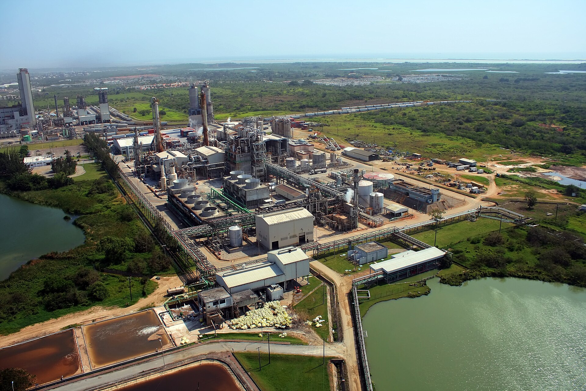 Aerial view of an industrial complex in the Altamira port corridor, Tamaulipas, surrounded by vegetation and bodies of water.